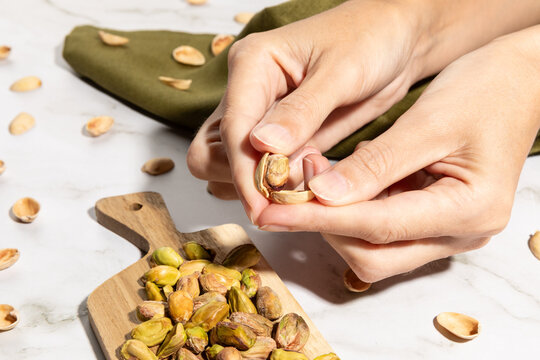 Close up of female hands peeling pistachio nuts on kitchen countertop surface