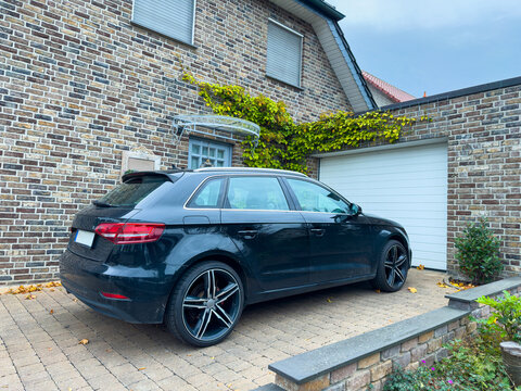 Elegant black car parked in a stylish driveway surrounded by brick walls and ivy in a quiet neighborhood on a cloudy day - Powered by Adobe