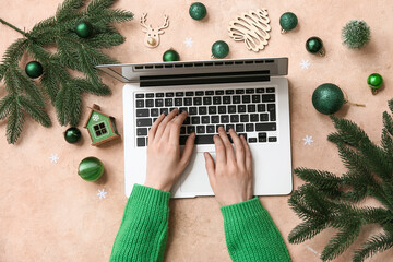 Female hands with modern laptop, fir branches and Christmas decorations on color background