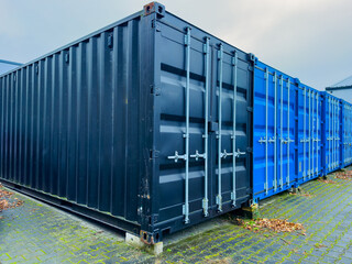 Colorful shipping containers lined up in a storage area during an overcast day, showcasing different textures and hues while surrounded by greenery