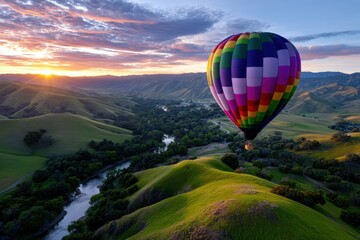 Fototapeta premium Colorful hot air balloon floats above green hills at sunset