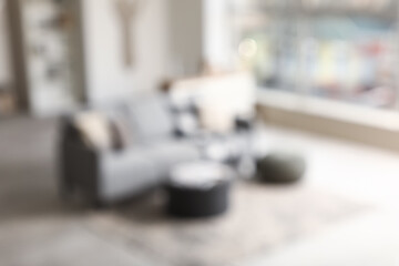 Stylish interior of living room with grey sofa and soft poufs, blurred view