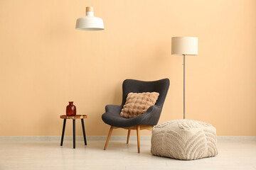 Stylish armchair with soft pouf and lamps near beige wall in modern room