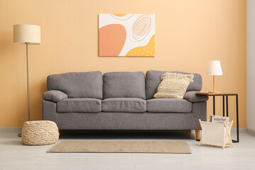 Stylish grey sofa with soft pouf and lamps near beige wall in living room