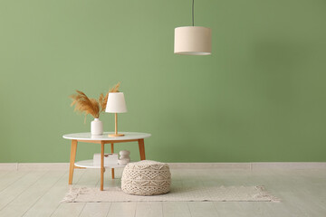 Table with soft pouf and stylish lamps near green wall in modern room