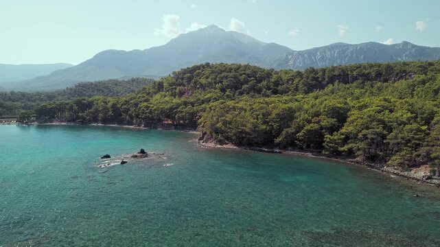 Drone view of Phaselis Bay with turquoise water, pine forest, and Mount Olympos in the background. Beautiful Mediterranean landscape near Kemer, Antalya, Turkey.