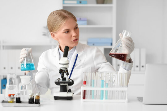 Female scientist with flasks and microscope working at table in laboratory