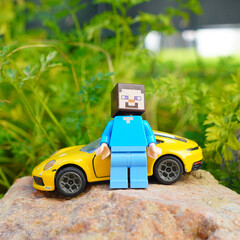 Obraz premium Minecraft Steve figure stands next to a yellow toy sports car on a rock