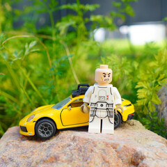 Naklejka premium Lego Star Wars figure with a yellow sports car on a rock in front of green foliage