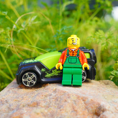 Obraz premium Lego minifigure farmer stands next to a toy car on a rock in a garden