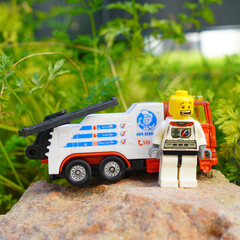 Obraz premium Astronaut figure stands next to a toy tow truck on a rock outdoors
