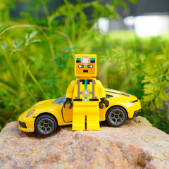 Obraz premium Lego figure stands next to a yellow toy car on a rock