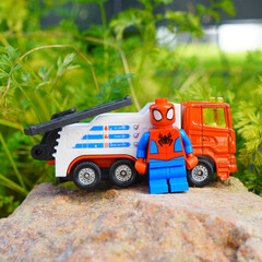 Obraz premium Spider-Man toy figure stands beside a tow truck on a rock outdoors