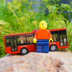 Obraz premium Lego minifigure stands next to a red toy bus on a rock