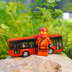 Obraz premium Lego Ninjago character stands next to a red toy bus on a rock