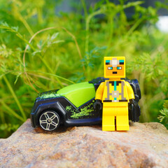 Naklejka premium Lego figure stands next to a toy car on a rock with a green background