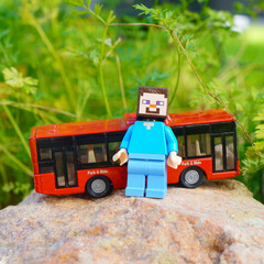 Naklejka premium Minecraft Steve figure with a red toy bus on a rock outdoors