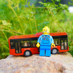 Naklejka premium Lego bus driver figure stands next to a red toy bus on a rock