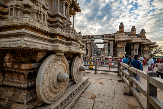 Hampi, India - 01 November 2025: View of the intricately carved stone chariot at Vittala Temple, bathed in warm light against a vibrant sky, showcasing ancient artistry.