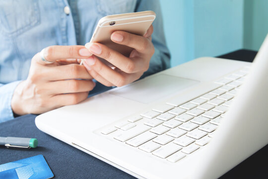 Close up image of woman's hands using smartphone and laptop computer on workspace desk, Space for text or design