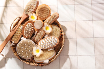Basket with different massage brushes and plumeria flowers on white tile background