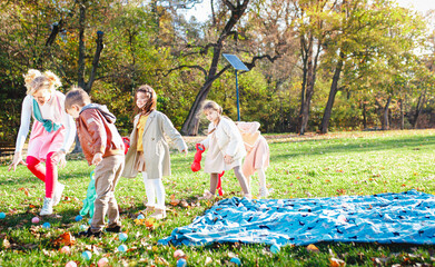 Group of happy kids with a female party animator laughing and playing with toys on the grass...