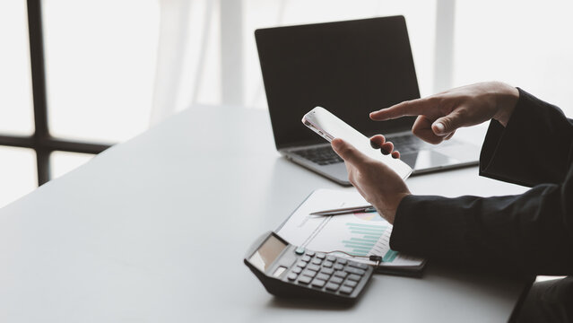 business person using smartphone with calculator and laptop on desk