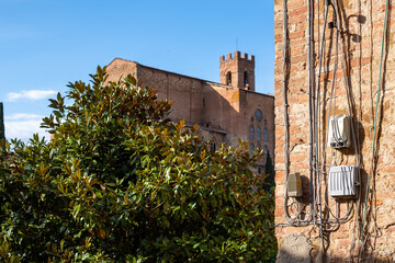 Obraz premium Electrical installation on a brick wall with visible wires and safety features, surrounded by greenery and historical architecture, showcasing urban infrastructure and design concepts