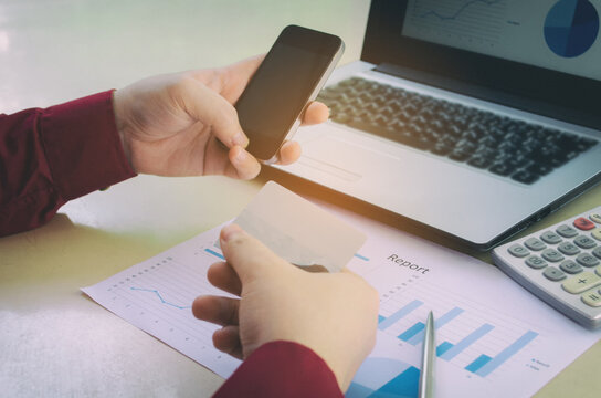 Business person making online payment using smartphone and credit card with financial report and laptop