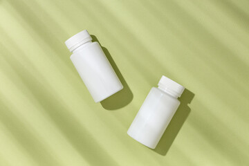 Blank plastic vitamin bottles on green background