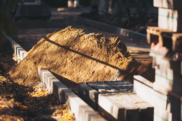 Construction site with a pile of dirt near laid bricks on a sunny day in a park setting