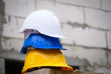 Raindrops on yellow, blue, white safety helmet placed on pile of bricks with house under construction background, construction problem concept.