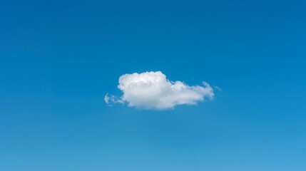 Lone fluffy white cloud drifts serenely across a vast, clear blue sky on a bright, sunny day