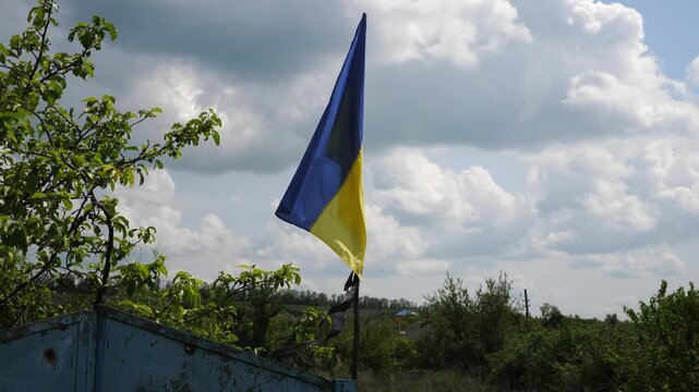 Blue-yellow flag waves proudly on a old fence in Kharkivska oblast. The scene symbolizes the resilience and unbroken spirit of the ukrainian people and the failure of invading russian forces