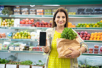 Indian woman showing smartphone screen at super shop.