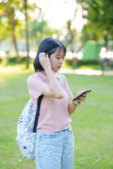 A young woman listens to music on her phone. An Asian woman stretches after sitting for a long time.