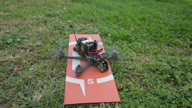 An FPV drone rests on a grass launch pad as the pilot switches it into arm mode, the motors giving a subtle twitch before liftoff.