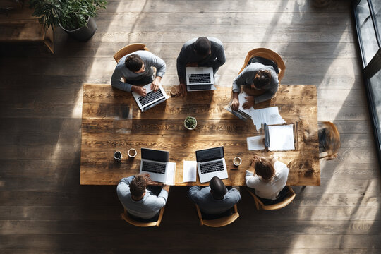 Top view of diverse business team working together at wooden table with laptops and documents in modern office, collaboration and teamwork concept