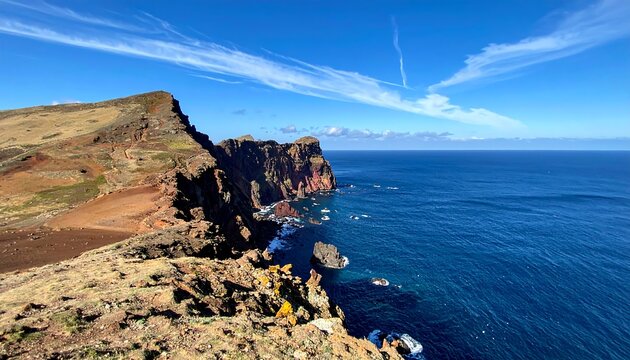 Rugged cliffs descend into deep blue ocean under a clear blue sky with wispy clouds, a serene coastal vista - Powered by Adobe