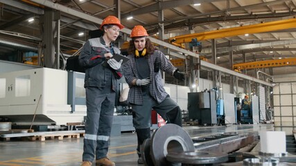 Young female metalworking factory technician explaining manufacturing process to middle aged colleague taking notes on digital tablet while collaborating in machine workshop - Powered by Adobe