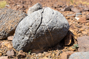 Rounded Grey Volcanic Boulder with Quartz Veins and Cracks on Reddish Desert Ground