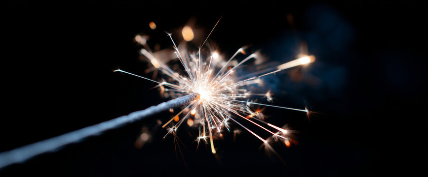 Close-up of a lit sparkler emitting bright sparks against a dark background with glowing light trails and dynamic energy