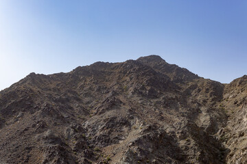 Steep, rugged slope of dark rocky mountain under a clear blue sky