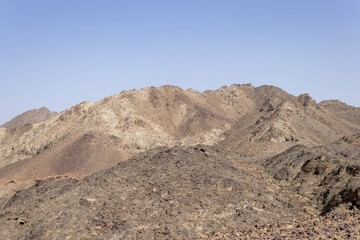 Vast, rugged desert landscape featuring layered, rocky mountains under a clear blue sky.