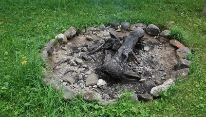 Obraz premium A circular fire pit with charred wood and blackened ashes, surrounded by smooth stones, reflecting a recent outdoor gathering