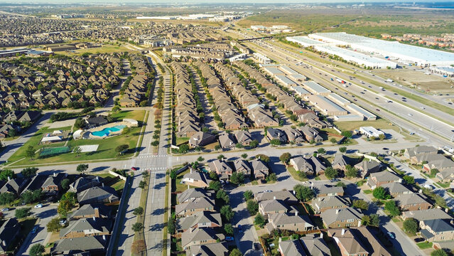 Highway stack interchange, pedestrian bridge, open plain from Castle Hills in Lewisville, TX with upscale two-story homes, median street, immature landscaping, HOA pool, tennis court, warehouse