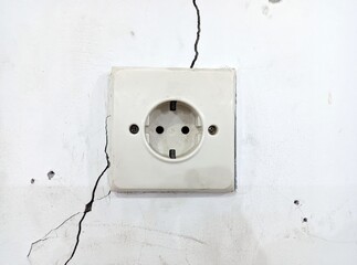 Old European electrical outlet on a damaged, cracked white wall, symbolizing danger and urgent need for repair.