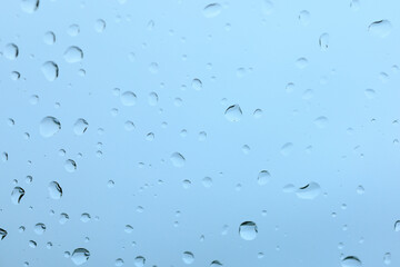 A macro, high-detail view of countless water droplets and streaks on a cool blue glass surface, creating a beautiful, abstract texture ideal for a wet weather background.