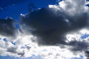 Himmellandschaft mit blauem Himmel und dramatischem schwarz-weißem Wolkengebilde mit Licht bei Sonne, Sturm und Regen am Nachmittag im Herbst