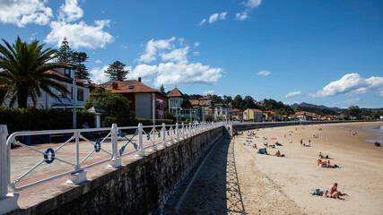 Fototapeta premium Sunny Day at a Coastal Beach with Promenade and Historic Houses in Ribadesella. Asturias. Spain